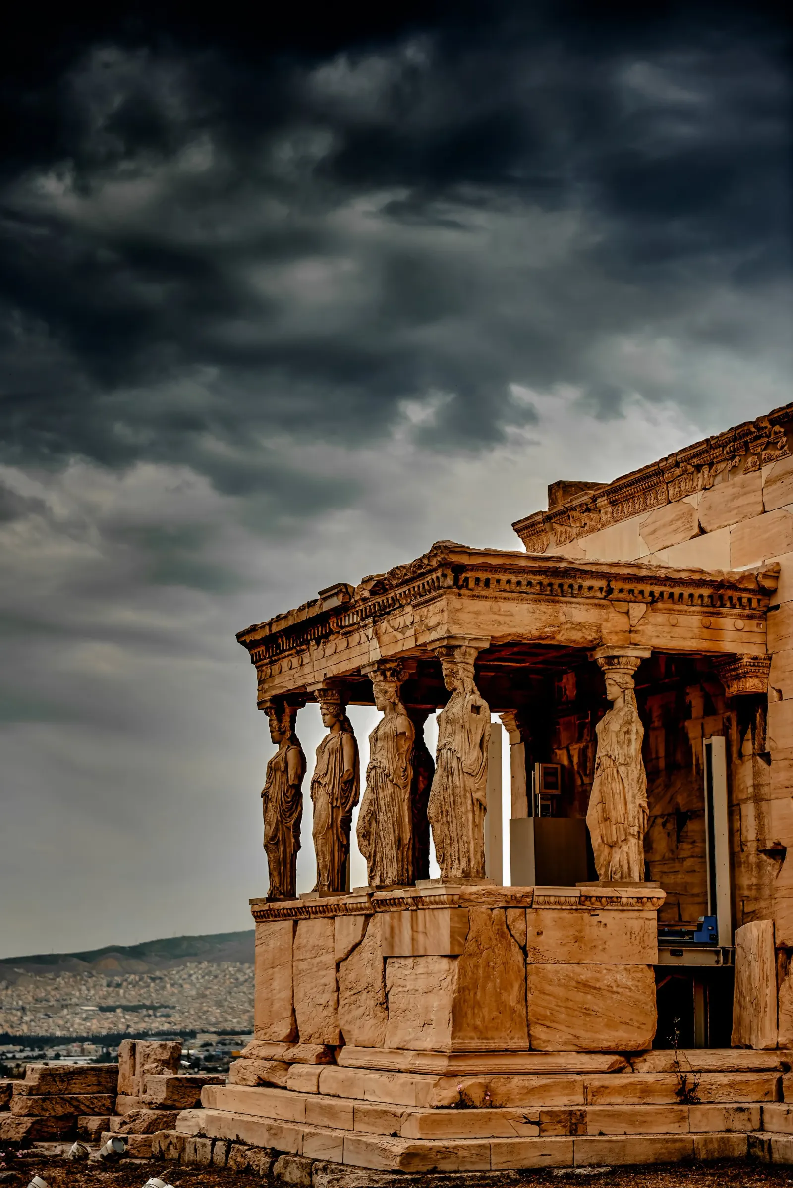 Stone caryatids supporting a porch on the Acropolis, under a dark storm sky.
